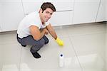 Portrait of a smiling young man cleaning the kitchen floor at house