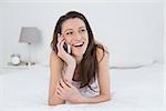 Cheerful young woman using mobile phone in bed at home