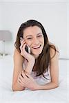 Portrait of a smiling young woman using mobile phone in bed at home