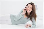 Relaxed smiling young woman using mobile phone in bed at home