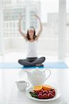 Blurred toned young woman sitting in meditation posture with healthy food in foreground at fitness studio