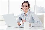 Portrait of a smiling businesswoman doing online shopping through laptop and credit card in office