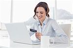 Smiling businesswoman doing online shopping through laptop and credit card in office