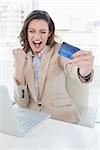 Excited businesswoman doing online shopping through laptop and credit card in office