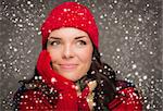 Happy Mixed Race Woman Wearing Winter Hat and Gloves Enjoys Watching the Snow Fall Looking to the Side on Gray Background.