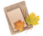 Brown paper notepad with pencil and autumn leaf over burlap. Isolated on white background