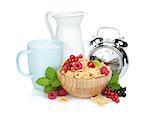 Fresh corn flakes with berries, milk jug, cup and alarm clock. Isolated on white background