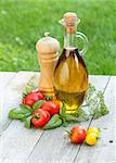 Olive oil bottle, pepper shaker, tomatoes and herbs on wooden table