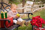Happy Young Toddler Child Sitting on Bench Holding Green Apple with Christmas Gifts Outside.