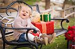 Happy Young Toddler Child Sitting on Bench with Christmas Gifts Outside.