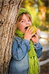 Cute Smiling Young Girl Wearing Green Scarf and Hat Eating A Green Apple Outside.