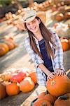 Preteen Girl Wearing Cowboy Hat Playing with a Wheelbarrow at the Pumpkin Patch in a Rustic Country Setting.