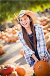 Preteen Girl Wearing Cowboy Hat Playing with a Wheelbarrow at the Pumpkin Patch in a Rustic Country Setting.