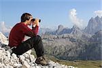 Young man looking through binoculars into the valley in the mountains