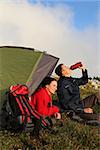 Young couple with a tent is watching the sunset in the mountains