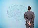 Composite image of businessman standing with hands behind back looking at fair brain on blue background