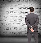 Composite image of businessman standing with hands behind back looking at brick lined wall