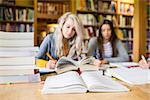 Two blurred students writing notes with stack of books at desk in the college library