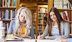 Two female students writing notes at desk in the college library