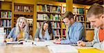 Group of four students writing notes at desk in the college library