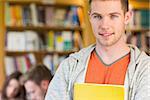 Portrait of a smiling male student with others in background in the college library