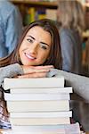 Portrait of a smiling female student with stack of books while others in background at the college library