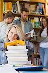 Portrait of a smiling female student with stack of books while others in background at the college library