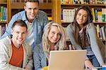 Group portrait of four happy students using laptop at desk in the college library