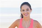 Close up portrait of a smiling healthy woman with earphones on beach