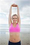 Beautiful smiling toned woman stretching hands over head on the beach