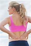 Rear view of a healthy woman in sports bra suffering from back pain on beach