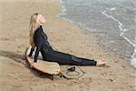 Side view of a beautiful blond in wet suit with surfboard at the beach