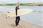 Full length side view of a beautiful young woman in wet suit holding surfboard at the beach