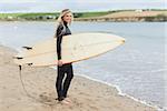 Full length portrait of a beautiful young woman in wet suit holding surfboard at the beach