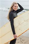 Portrait of a beautiful young woman in wet suit holding surfboard at the beach