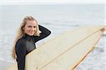 Portrait of a beautiful young woman in wet suit holding surfboard at the beach