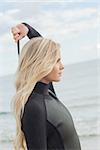 Side view of a young blond in wet suit standing at the beach