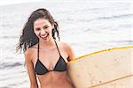 Portrait of a cheerful young bikini woman holding surfboard at beach