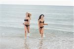 Portrait of two smiling young bikini women running in water at the beach