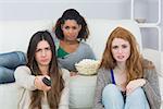 Portrait of serious young female friends with remote control and popcorn bowl on sofa at home