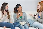 Cheerful young female friends with wine glasses and popcorn enjoying a conversation on sofa at home