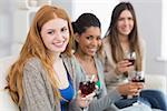 Portrait of smiling young female friends with wine glasses sitting on sofa at home