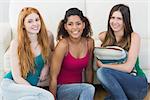 Portrait of cheerful young female friends on floor against sofa at home