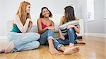 Happy young female friends enjoying a conversation on floor against sofa at home