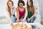 Happy young female friends eating pizza on sofa at home