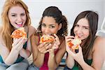 Portrait of happy young female friends eating pizza on sofa at home