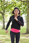 Portrait of a beautiful healthy young woman in black jacket jogging in the park