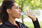 Close up side view of a tired healthy young woman drinking water in the park