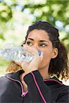 Close up of a tired healthy young woman drinking water in the park