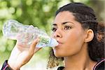 Close up of a tired healthy young woman drinking water in the park